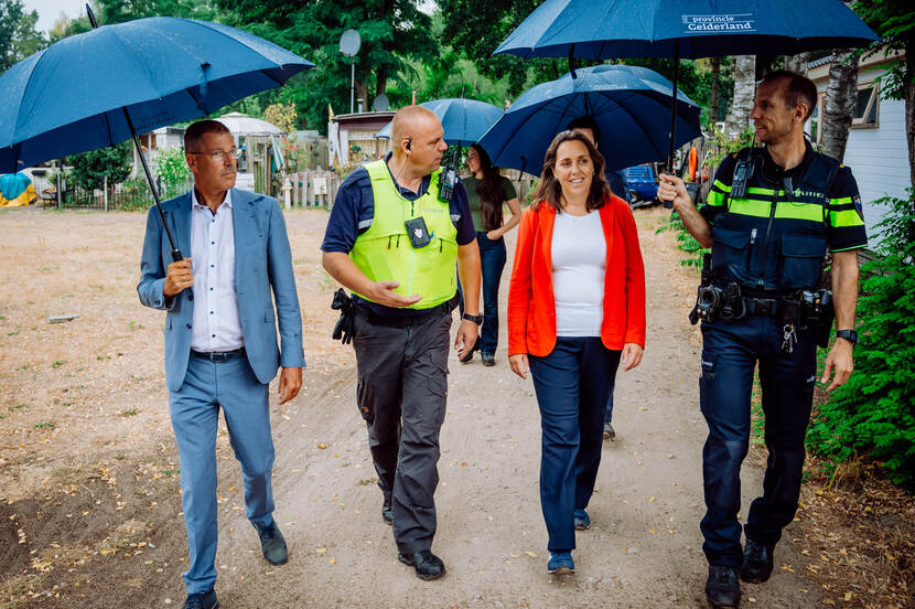 Een directeur van het ministerie van Justitie en Veiligheid (JenV), een gedeputeerde van de provincie, een politieagent en een toezichthouder van het Ariadne-project lopen door een vakantiepark.