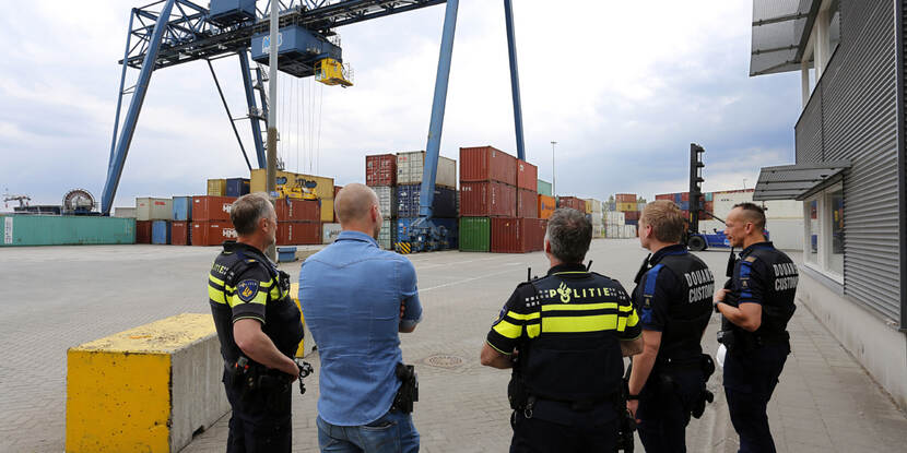 Politieagenten en Douane kijken naar containers in een haven.