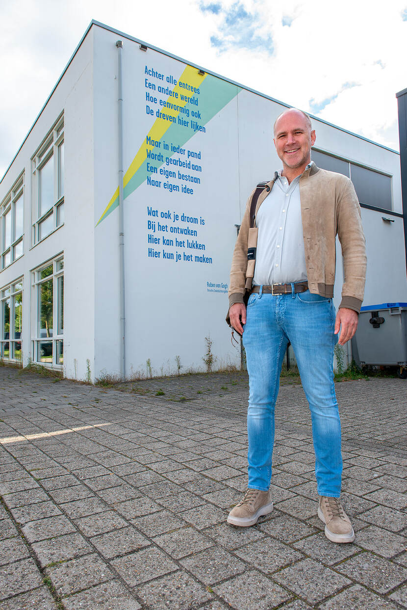 Ondernemer Bob Scherrenberg staat voor een gebouw met daarop een muurgedicht