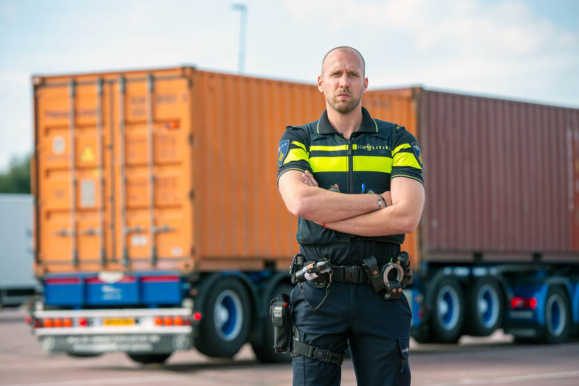 Kernlid Tom Torensma van de politie staat met zijn armen over elkaar en kijkt de camera in, op de achtergrond staat een vrachtwagen