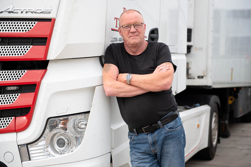 Vrachtwagenchauffeur Don de Wilde staat tegen de zijkant van een vrachtwagen geleund met zijn armen over elkaar en kijkt de camera in