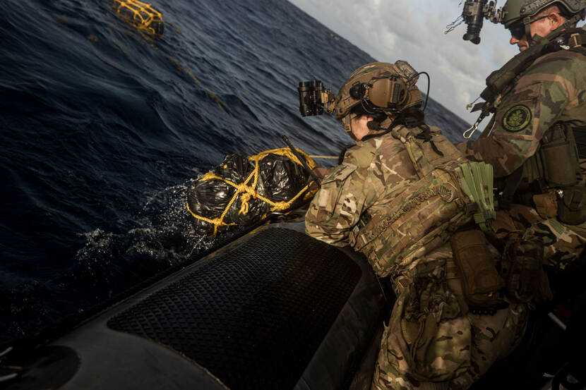 Twee medewerkers van Defensie op een boot vissen een zwarte vuilniszak uit het water.