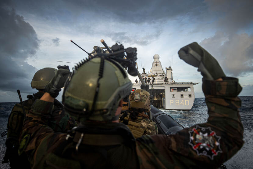 Medewerkers van defensie staan op een boot met vuisten omhoog. Ze kijken naar een andere boot waarop andere medewerkers staan te klappen.