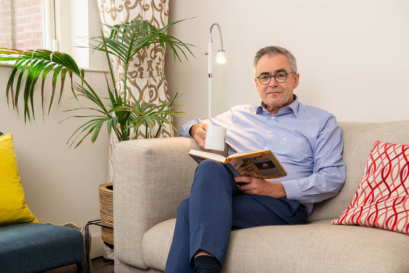 Burgemeester Jos Wienen zit op een bank met een mok drinken in zijn rechterhand en een boek in zijn linkerhand