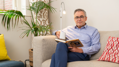 Burgemeester Jos Wienen zit op een bank met een mok drinken in zijn rechterhand en een boek in zijn linkerhand