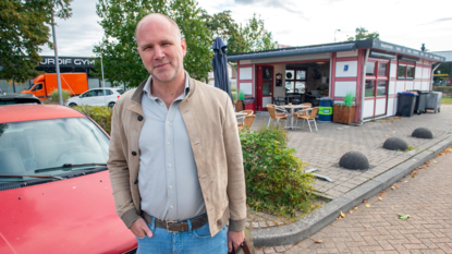 Ondernemer Bob Scherrenberg staat voor een rode auto en kijkt in de camera